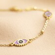 Close Up of Lilac Enamel Evil Eye Anklet in Gold on Beige Fabric 