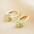 Green Beaded Flower Charm Huggie Hoops in Gold on neutral coloured fabric