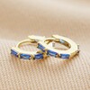 Blue Baguette Crystal Huggie Hoops in Gold on neutral coloured fabric