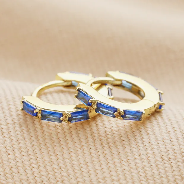 Blue Baguette Crystal Huggie Hoops in Gold Blue Baguette Crystal Huggie Hoops in Gold on neutral coloured fabric
