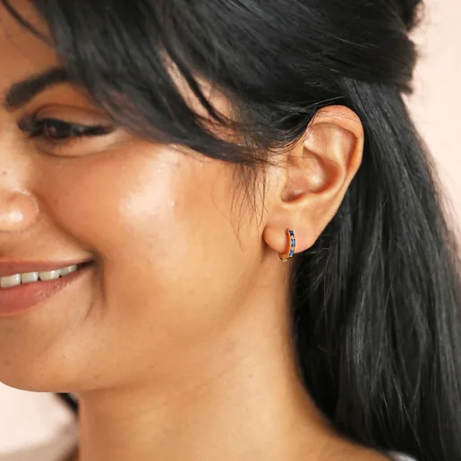 Model smiling wearing Blue Baguette Crystal Huggie Hoops in Gold