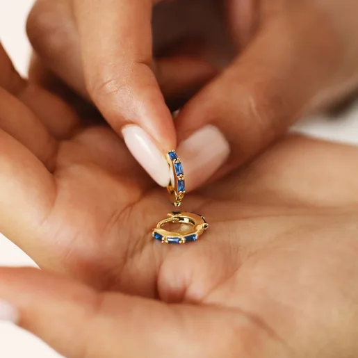 Model holding Blue Baguette Crystal Huggie Hoops in Gold in palm of hand