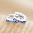 Blue Baguette Crystal Huggie Hoops in Silver stacked on neutral coloured fabric