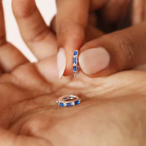 Model holding Blue Baguette Crystal Huggie Hoops in Silver in palm of hand