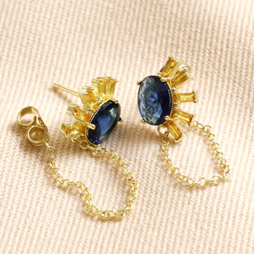 Blue Crystal Sunburst and Chain Stud Earrings in Gold Blue Crystal Sunburst and Chain Stud Earrings in Gold With Butterfly Backs Detached on Beige Fabric