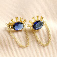 Blue Crystal Sunburst and Chain Stud Earrings in Gold on Beige Fabric 