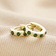 Huggies from Set of 2 Green Crystal Huggie and Hoop Earrings in Gold on top of beige coloured material