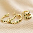 Set of 2 Green Crystal Huggie and Hoop Earrings in Gold laid out on top of neutral coloured fabric