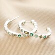 Hoops from Set of 2 Green Crystal Huggie and Hoop Earrings in Silver on top of neutral coloured material