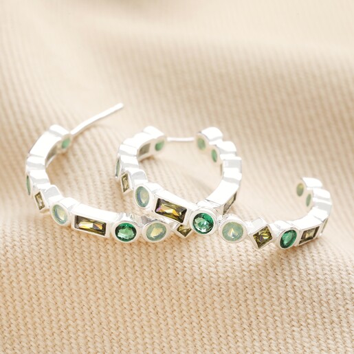 Hoops from Set of 2 Green Crystal Huggie and Hoop Earrings in Silver on top of neutral coloured material