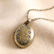 Antiqued Crystal Star Oval Locket Necklace in Gold laid out on top of beige coloured material