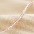 Close Up of Delicate Rose Quartz Stone Beaded Necklace on Beige Fabric