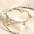 Blue Seed Bead Star and Pearl Charm Necklace in Gold arranged on top of neutral coloured fabric