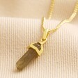Close up of Labradorite Crystal Point Pendant Necklace in Gold against neutral coloured material