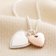 Mixed Metal Textured Double Heart Necklace in Silver laid out on top of beige coloured fabric