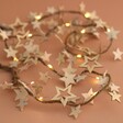 Battery Powered LED Wooden Star Garland lit up and arranged on natural coloured backdrop