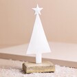 White Enamel Christmas Tree Ornament on Beige Background with Snow Scattered at Base