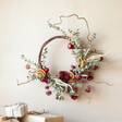 Fruitcake Dried Flower Wreath Hanging on Cream Wall with Wrapped Gifts Underneath 