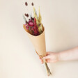 Mulled Wine Dried Flower Bouquet in Paper Held by Model Against Beige Wall