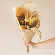 Model holding Coastal Shades Dried Flower Bouquet in packaging against neutral coloured background