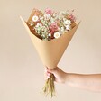 Model holding Pink Daisy Dream Dried Flower Bouquet in packaging against neutral wall