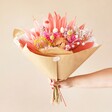 Model holding the Tutti Frutti Dried Flower Bouquet wrapped in brown paper in front of pink background
