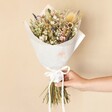 Wildflower Dried Flower Wedding Bouquet Wrapped in White Paper and Held Against Beige Background by Model