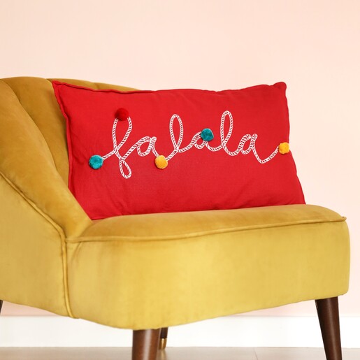 Falala Embroidered Red Pom Pom Cushion on top of mustard coloured chair with neutral coloured background
