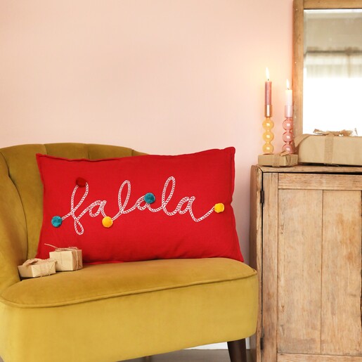 Lifestyle shot of Falala Embroidered Red Pom Pom Cushion on top of mustard coloured chair
