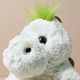 Close up of Warmies Marshmallow Green Dinosaur Soft Toy against neutral coloured background