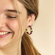 Model Smiling wearing My Doris Large Rainbow Hoop Earrings in Gold against neutral background
