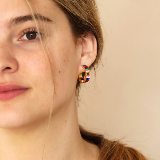 Model looking forward wearing My Doris Medium Rainbow Hoop Earrings in Gold against neutral backdrop