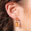 A pair of drop earrings with a clear oval crystal atop a rectangular amber gemstone close up on models ear