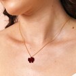 A red velvet bow pendant attached to a thin gold trace chain close up on models chest