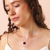 A red velvet bow pendant attached to a thin gold trace chain shown on models chest