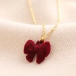 A red velvet bow pendant attached to a thin gold trace chain 