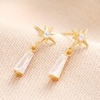 Star and Crystal Drop Earrings in Gold Against Beige Background