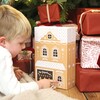 A large card advent calendar designed to look like a gingerbread bakery with 24 square compartments being played with by child model