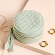 Quilted Round Mini Travel Jewellery Case closed and ripped up against a beige background