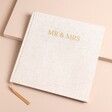 A natural colour linen book on a neutral background with the words 'Mr & Mrs' in captital letters and gold foil at the front top centre