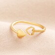 A slim banded adjustable gold ring with two hearts on either end, one of which is a block out heart and the other is an outline.