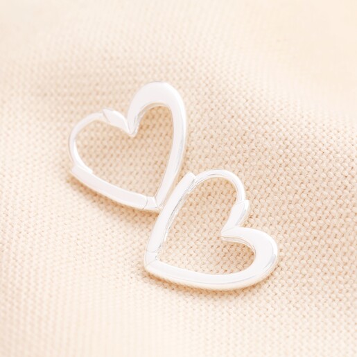 Sterling Silver Heart Outline Huggie Hoop Earrings on a Beige Background. Sterling Silver Heart Outline Huggie Hoop Earrings