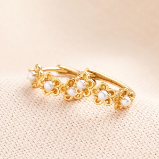 Sterling Silver Pearl Flower Huggie Hoop Earrings in Gold on a Beige Background. A small pair of huggie earrings with three gold flowers and pearl centres