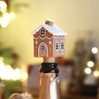 A Resin Gingerbread House Bottle Stopper Inside the Neck of a Bottle of Wine in Front of Christmas Tree