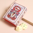 White and Green Speckled Chocolate Frog Next to a Vintage Decorated Box on a Neutral Background