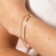 A double layer gold bracelet with a herringbone chain as well as a trace chain threaded with five imitation pearls spread around close up on a model