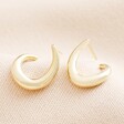 Illusion Swirl Hoop Earrings in Gold on a Beige Background.