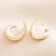 Illusion Swirl Hoop Earrings in Gold on a Beige Background.
