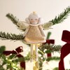 An angel Christmas tree topper with white hair in two low buns either side of her face and a golden crown atop. She has gold and silver mesh wings and a sparkling gold dress adorned with sequins. She wears a pearl necklace and has gold and silver ballet p