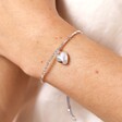 Close Up of Semi Precious Beaded Heart Charm Cord Bracelet in Silver on Model on a Beige Background.